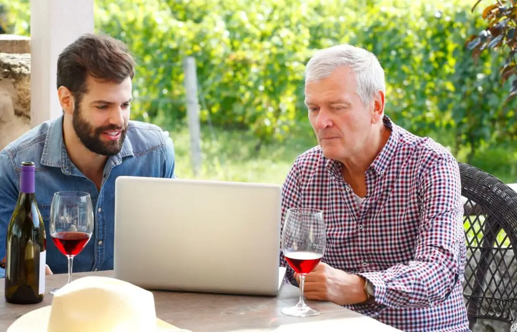 Due imprenditori esaminano i conti al portatile con un calice di vino
